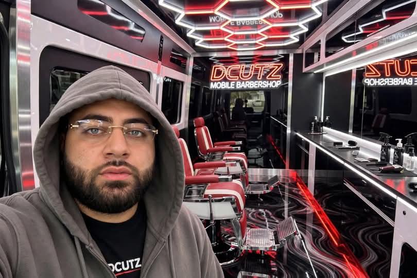 The DCUTZ barber taking a selfie in front of the red barber chairs and neon sign